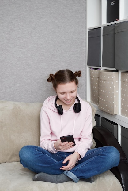 Jovem feliz usa telefone celular enquanto está sentado em posição de lótus no sofá em casa