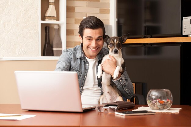 Jovem feliz usando laptop enquanto segura cachorro em casa