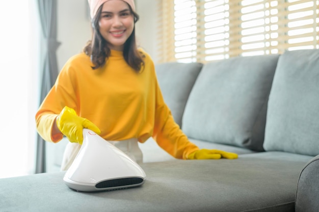 Jovem feliz usando luvas amarelas e aspirador Limpando um sofá na sala de estar