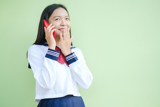 Jovem feliz usando smartphone em fundo verde, menina asiática, menina da escola.