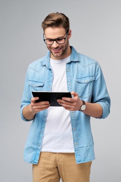 Jovem feliz vestindo camisa jeans em pé e usando tablet