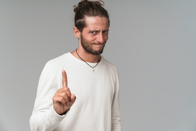 Jovem feliz vestindo roupas casuais, isolado em uma cinza, apontando o dedo para o espaço da cópia