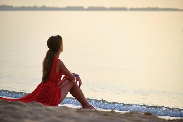 Jovem feliz vestindo vestido vermelho descansando na praia do mar aproveitando a manhã quente de verão