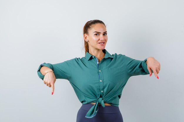 Foto jovem fêmea linda apontando para baixo em camisa verde e olhando alegre, vista frontal.