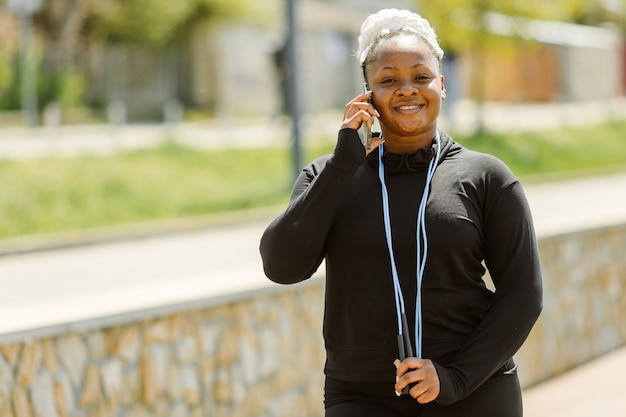 Jovem fêmea se divertindo treinando ao ar livre. Conceito de estilo de vida de pessoas desportivas. Mulher em roupas esportivas falando ao telefone