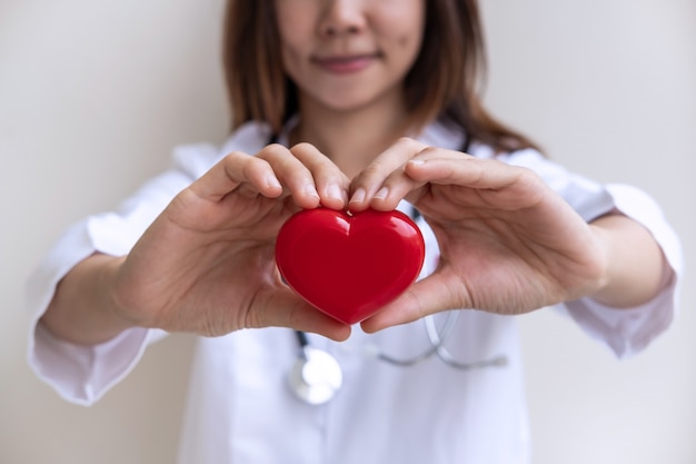 Jovem, femininas, doutor, com, a, estetoscópio, segurando, coração vermelho, cardiolog, cuidado saudável, conceito