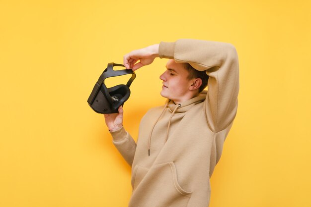 Jovem fica em um fundo amarelo e usa um capacete de realidade virtual Retrato de cara positivo com capacete VR no fundo da parede amarela Conceito de jogo VR