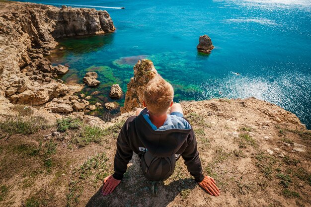 Jovem fica em um penhasco alto com vista para os arcos de penhascos rochosos e água do mar azul-turquesa