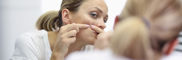 Jovem fica na frente do espelho e pressiona espinhas com o retrato de mãos. Conceito de limpeza em casa para cuidados com a pele facial