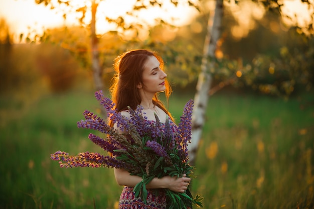 Jovem ficar no campo com vista para o campo de lavanda. Sorrindo despreocupada garota caucasiana em vestido, apreciando o pôr do sol