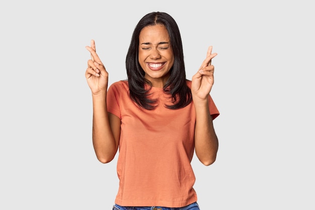 Jovem filipina com longos cabelos pretos no estúdio cruzando os dedos por ter sorte
