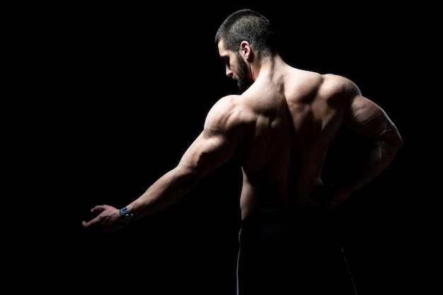 Jovem fisiculturista flexionando os músculos isolar no espaço de cópia preto preto