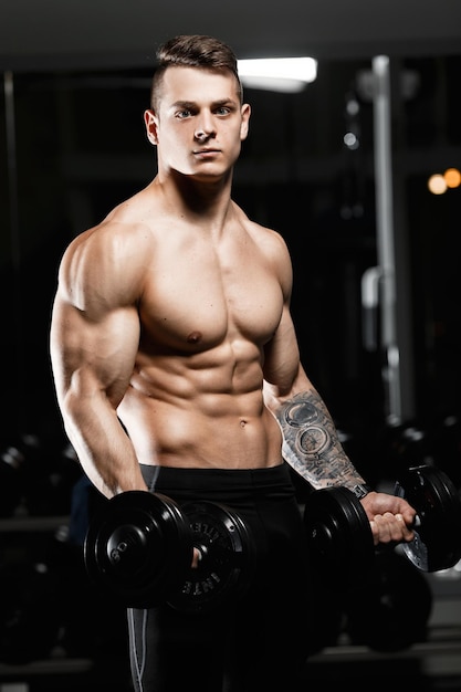 Jovem fisiculturista masculino atraente mostra músculos no ginásio O atleta Professional Light