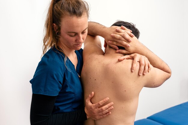 Jovem fisioterapeuta caucasiana dando massagem nas costas a um paciente sentado em uma maca