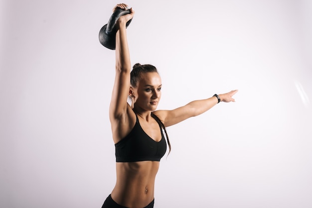 Jovem fitness com corpo musculoso perfeito levantando o kettlebell acima da cabeça