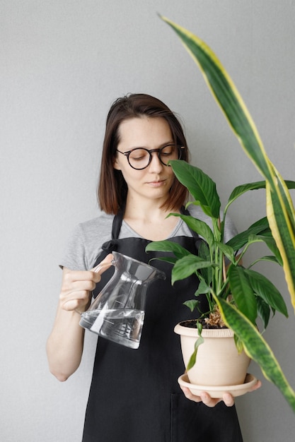 Jovem florista branca com uma camiseta e um avental escuro na floricultura de sua casa segurando uma cesta