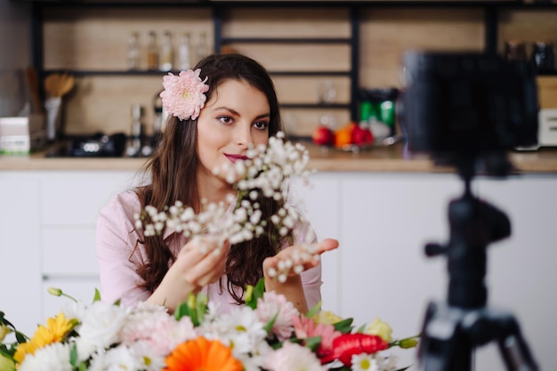 Jovem florista grava tutorial em vídeo de design de composições florais na câmera designer de interiores mulher grava vlog na câmera organiza decorações de flores artesanais