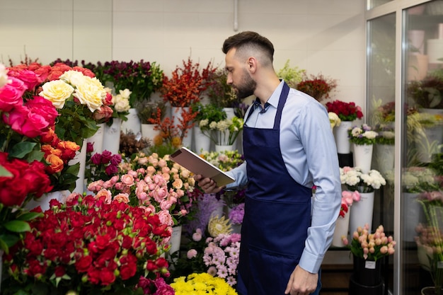 jovem florista masculino dentro de uma geladeira de flores examina buquês.