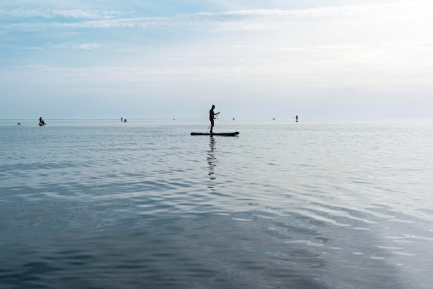 Jovem flutuando na prancha de stand up paddle no mar no dia ensolarado de verão ativo estilo de vida atividade ao ar livre