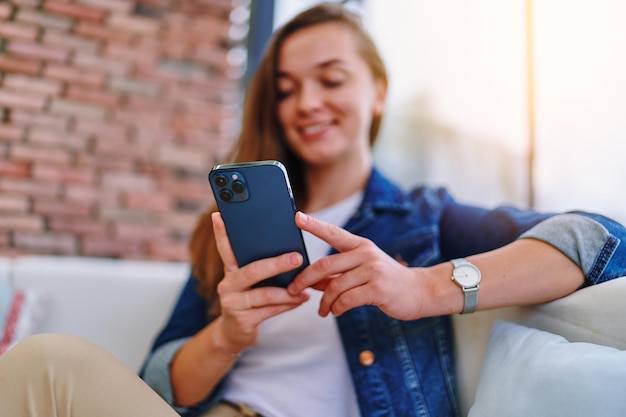 Jovem fofa feliz alegre sorridente mulher moderna inteligente usando telefone celular para navegar, assistir a vídeos online, bater papo e redes sociais no café