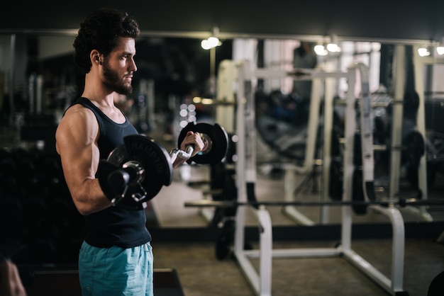 Jovem forte e barbudo com corpo musculoso e musculoso, vestindo roupas esportivas e malhando com barra