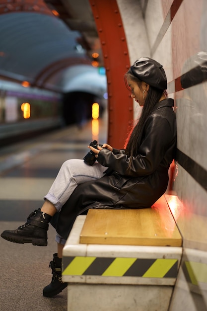 Jovem fotógrafa asiática feminina segurando uma câmera olhando a fotografia esperando o metrô