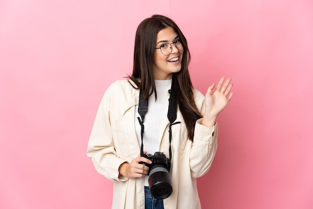 Jovem fotógrafa brasileira isolada saudando com a mão com expressão feliz