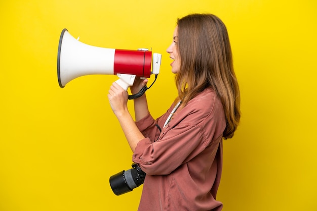 Jovem fotógrafa caucasiana isolada em fundo amarelo gritando através de um megafone