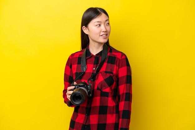 Jovem fotógrafa chinesa isolada em fundo amarelo olhando de lado