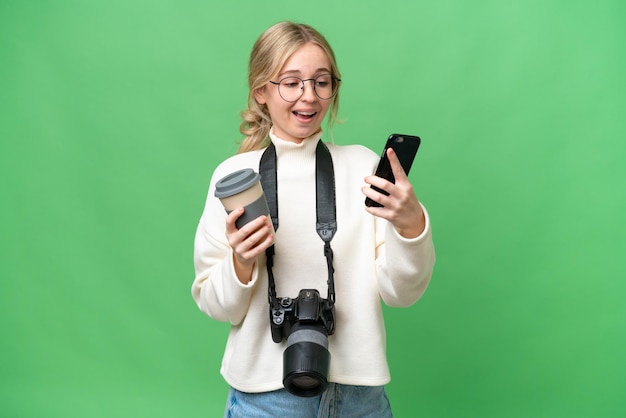 Jovem fotógrafa inglesa sobre fundo isolado segurando café para levar e um celular