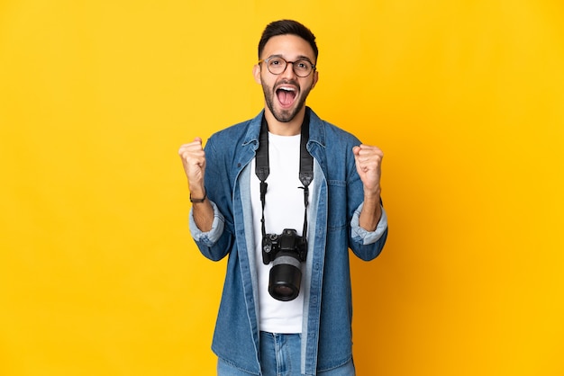 Jovem fotógrafa isolada em um fundo amarelo comemorando uma vitória na posição de vencedora