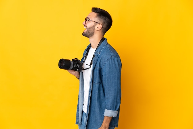 Jovem fotógrafa isolada em um fundo amarelo rindo em posição lateral