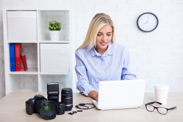 Jovem fotógrafa sentada com computador e equipamento fotográfico em um escritório moderno