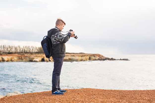 Jovem fotógrafo com mochila fazendo fotos de mar e pedras com a câmera. Mar Mediterrâneo