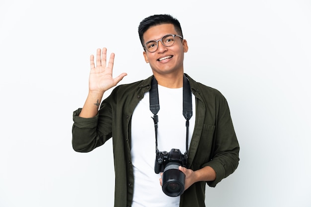 Jovem fotógrafo equatoriano isolado no fundo branco saudando com a mão com expressão feliz