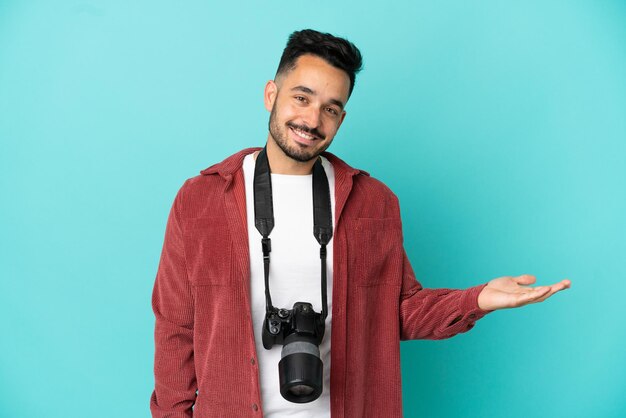 Jovem fotógrafo homem caucasiano isolado em um fundo azul apresentando uma ideia enquanto olha sorrindo para