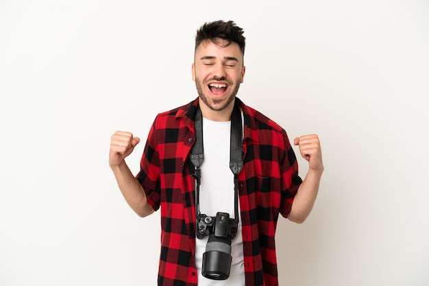 Jovem fotógrafo homem caucasiano isolado no fundo branco comemorando vitória na posição de vencedor