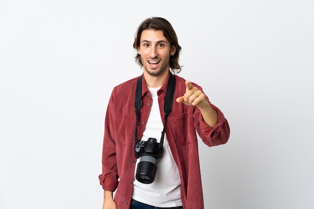 Jovem fotógrafo isolado na parede branca surpreso e apontando para a frente