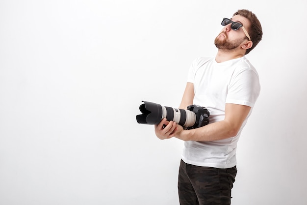 Jovem fotógrafo profissional de camisa branca segura uma câmera digital pesada com uma lente longa. trabalho duro