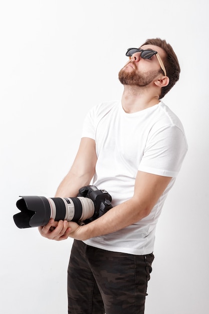 Jovem fotógrafo profissional de camisa branca segura uma câmera digital pesada com uma lente longa. trabalho duro