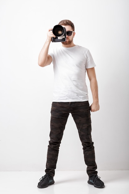 Jovem fotógrafo profissional de sucesso em camiseta branca usa câmera digital com lente longa. fotógrafo pronto para fotografar