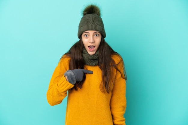 Jovem francesa isolada em um fundo azul com chapéu de inverno e expressão facial surpresa