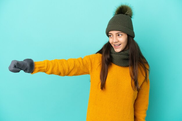 Jovem francesa isolada em um fundo azul com chapéu de inverno fazendo um gesto de polegar para cima