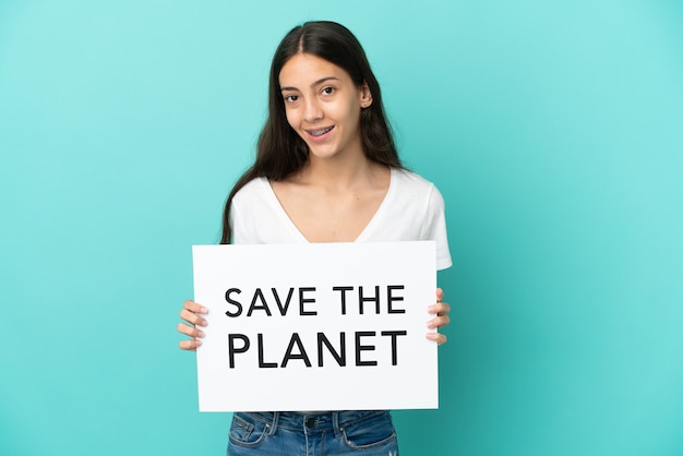 Jovem francesa isolada em um fundo azul segurando um cartaz com o texto Salve o Planeta com uma expressão feliz