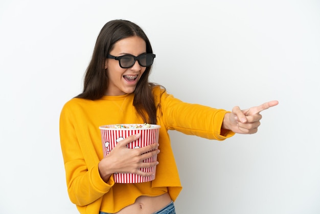 Jovem francesa isolada no fundo branco com óculos 3D e segurando um grande balde de pipocas enquanto aponta para longe