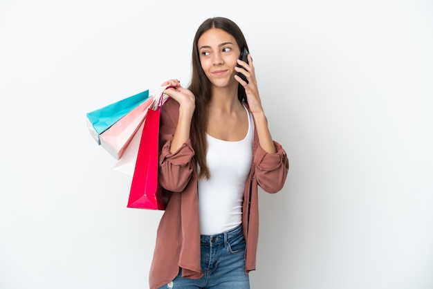 Jovem francesa isolada no fundo branco segurando sacolas de compras e ligando para um amigo com o celular