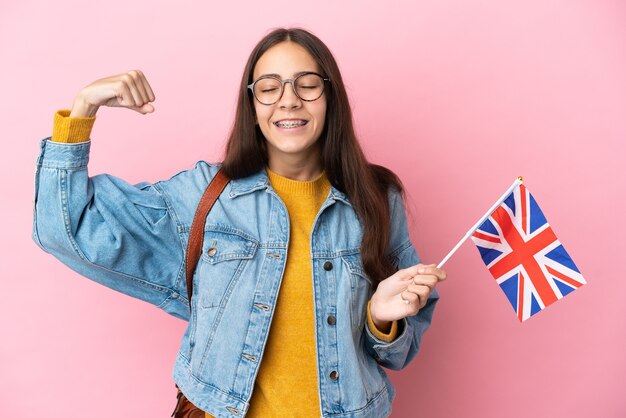 Jovem francesa segurando uma bandeira do reino unido isolada em um fundo rosa fazendo um gesto forte