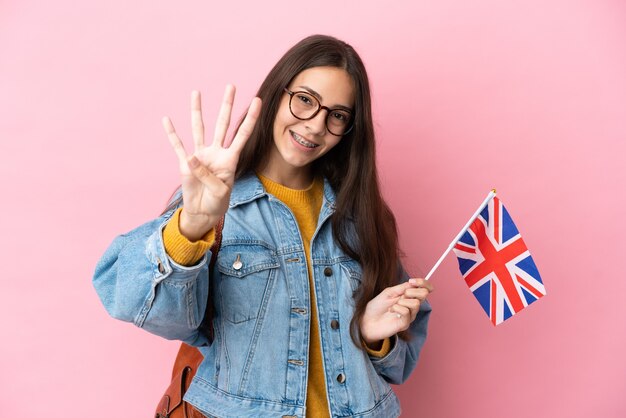 Jovem francesa segurando uma bandeira do Reino Unido isolada em um fundo rosa feliz e contando quatro com os dedos