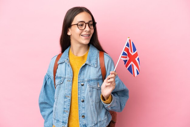 Jovem francesa segurando uma bandeira do Reino Unido isolada em um fundo rosa, olhando de lado