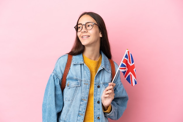 Jovem francesa segurando uma bandeira do Reino Unido isolada em um fundo rosa pensando em uma ideia enquanto olha para cima